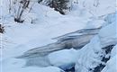 A narrow river flows through a winter landscape with a lot of snow. Some snow-covered rocks lie on the shore.