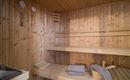 Eine gemütliche Sauna mit Holzverkleidung. Auf den Bänken liegen Handtücher bereit, während die Temperatur und Luftfeuchtigkeit gemessen werden.