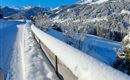 Eine verschneite Landschaft mit Bergen im Hintergrund und klarem blauem Himmel. Der Weg ist von frischem Schnee bedeckt.