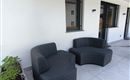 Eine moderne Terrasse mit zwei eleganten, grauen Sitzmöbeln. Im Hintergrund sind Fenster und Pflanzenkästen zu sehen.