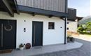 Ein modernes Haus mit Holzverkleidung und zwei Eingängen. Der gepflasterte Weg führt zur Terrasse und in den Garten.