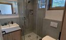 Ein modernes Badezimmer mit einer bodengleichen Dusche und einem Waschbecken. Große Fenster sorgen für viel Tageslicht und eine angenehme Atmosphäre.