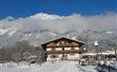 A picturesque chalet in the snowy landscape, surrounded by mountains. The sky is blue and sunny, creating a winter idyll.