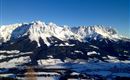 Eine beeindruckende Berglandschaft mit schneebedeckten Gipfeln und klarem blauen Himmel. Im Vordergrund sind grüne Täler zu sehen.