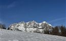 A snow-covered landscape with high mountains in the background. The sky is clear and blue.