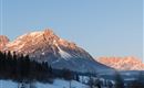 Eine beeindruckende Berglandschaft mit schneebedeckten Gipfeln und klarem Himmel. Die Sonne beleuchtet die Berge und schafft eine malerische Atmosphäre.