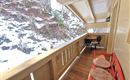 A cozy balcony with a red seating area and a small table. In the background, snow-covered mountains are visible.
