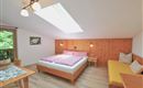 A cozy room with a double bed and a seating area. The walls are made of wood and a skylight provides plenty of daylight.