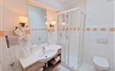 A modern bathroom with a shower, sink, and toilet. It is bright and friendly with tiles in white and orange.