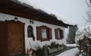 A traditional house in the snow, surrounded by a winter landscape. The layer of snow gently rests on the roof and the plants.