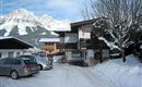 A snowy mountain village with modern houses and snow-covered streets. Majestic mountains rise in the background under a clear sky.