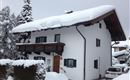A white house in the snow with a balcony and green windows. The garden is festively covered with a thick layer of snow.