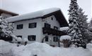 A cozy house in the snow with a beautiful balcony.  
Surrounded by snow-covered trees and a wintry landscape.