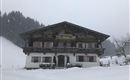 Ein traditionelles Chalet im Schnee, umgeben von einer winterlichen Landschaft. Die Flocken fallen sanft und verleihen der Szene eine ruhige Atmosphäre.