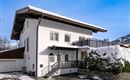 A modern house with a white facade and a balcony. The winter has covered the surroundings with snow.