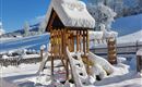 A playground in winter, covered with snow. The structures are hidden under a thick layer of snow and the landscape is snowy.