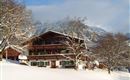 A beautiful chalet in the snowy landscape. In the background, mountains and trees can be seen.