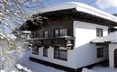A cozy house in the snow with a classic wooden roof. The surroundings are covered in fresh, white snow.