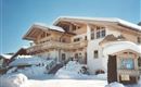 An elegant chalet in the snow with a spacious balcony. The entrance is surrounded by a picturesque snowy landscape.