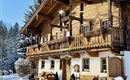 A cozy wooden house in winter, surrounded by snow and fir trees. The balconies are decorated with Christmas ornaments.