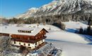 Ein charmantes Holzhaus im Schnee mit Blick auf majestätische Berge. Die Umgebung ist winterlich und, mit weißem Schnee bedeckt.