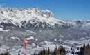 Eine winterliche Berglandschaft mit schneebedeckten Gipfeln und einem klaren blauen Himmel. Im Vordergrund steht ein Hinweiszeichen mit einer Geschwindigkeitsbezeichnung.