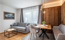 Ein modernes Wohnzimmer mit einem grauen Sofa und einem Holztisch. Große Fenster sorgen für viel Tageslicht und eine angenehme Atmosphäre.