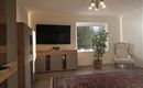 A modern living room with a large television on the wall. A cozy armchair and a plant create an inviting atmosphere.