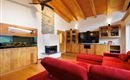 Ein modernes Wohnzimmer mit rotem Sofa und Holzwänden. Ein Aquarium, großer TV und ein Kamin verleihen dem Raum eine gemütliche Atmosphäre.