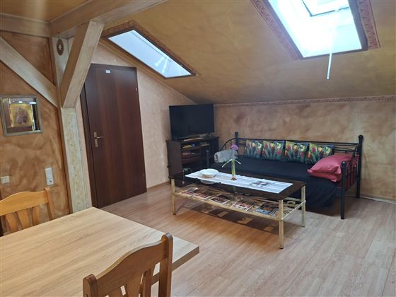 A cozy living space with a table, a sofa, and a television. There are skylights that let in plenty of light.
