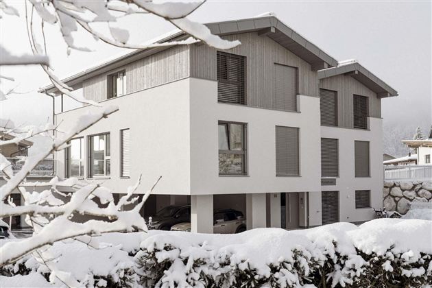 Ein modernes Haus im Winter, umgeben von Schnee. Die Architektur kombiniert Holz und Weiß und wirkt gleichzeitig gemütlich und stilvoll.