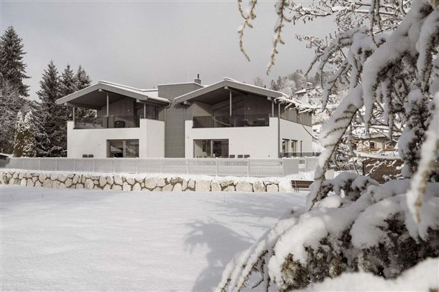 Ein modernes Haus im Schnee mit großen Fenstern und einem klaren Design. Umgeben von schneebedeckten Bäumen und einer ruhigen Winterlandschaft.