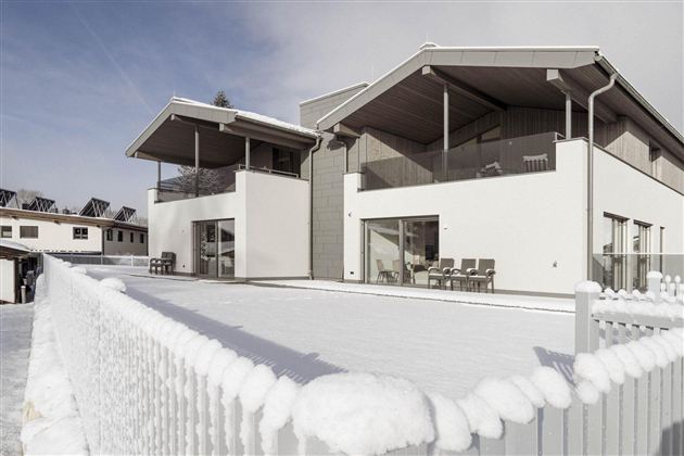 Ein modernes Haus mit Schnee bedeckt. Es hat große Fenster und einen gemütlichen Balkon.