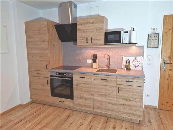 A modern kitchen made of wood with a countertop and a stove. It features a refrigerator and a microwave, as well as an elegant sink.