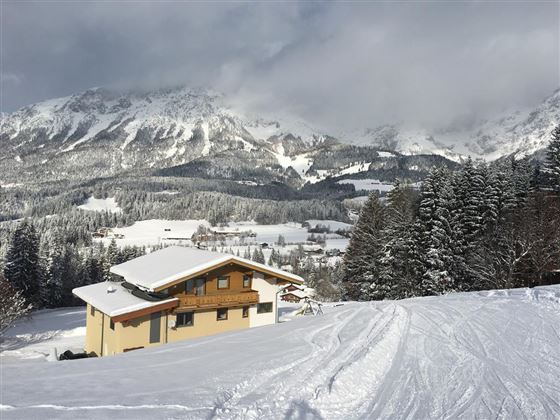 A modern house in a snow-covered landscape with impressive mountains in the background. The scenery conveys a calm winter atmosphere.