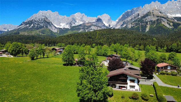 A picturesque landscape with green meadows and mountains in the background. Here are some buildings and trees that create a peaceful atmosphere.