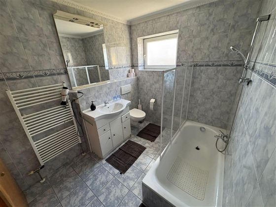 A modern bathroom with shower and bathtub.  
Tiles in gray and a large mirror create a bright atmosphere.