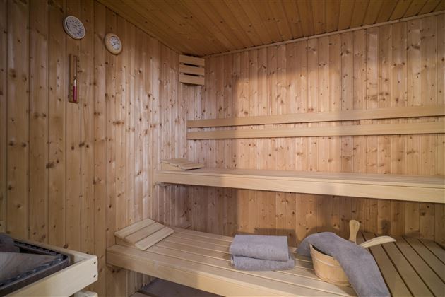Eine gemütliche Sauna mit Holzverkleidung. Auf den Bänken liegen Handtücher bereit, während die Temperatur und Luftfeuchtigkeit gemessen werden.