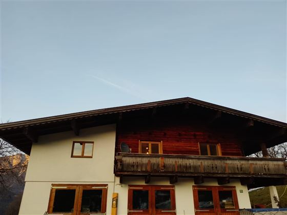 Ein traditionelles alpenländisches Haus mit einem Holz-Balkon. Der Himmel ist klar und blau.