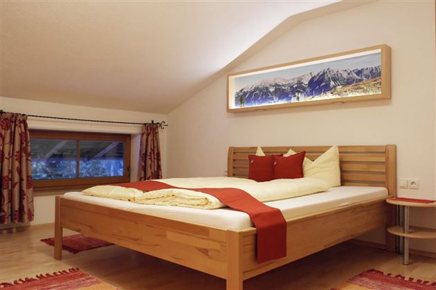 Een gezellige slaapkamer met een groot bed en moderne houten meubels. De kamer heeft een warme sfeer en een raam met uitzicht op de bergen.