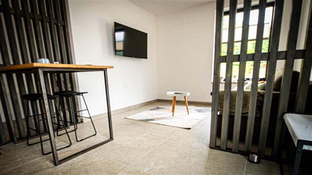 Ein modernes Wohnzimmer mit einem Fernseher an der Wand. Es gibt einen Esstisch mit Stühlen und einen kleinen Teppich auf dem Boden.