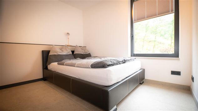 Ein einfaches Schlafzimmer mit einem Bett und zwei Kissen. Ein Fenster lässt natürliches Licht herein.