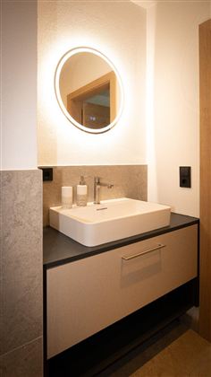 Ein modernes Badezimmer mit einem stilvollen Waschbecken und einem beleuchteten Spiegel. Die Einrichtung ist minimalistisch und elegant gestaltet.