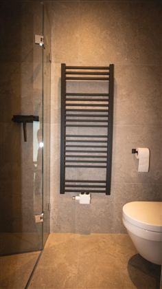 Ein modernes Badezimmer mit einer Glasdusche und einem Handtuchwärmer. Die Wände sind mit grauen Fliesen ausgekleidet, und ein WC ist sichtbar.