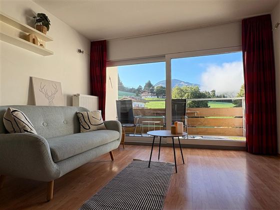 Mooi woonkamer met een grijze bank en grote ramen die uitzicht op de bergen bieden. De ruimte heeft lichte muren en stijlvolle decoratie.