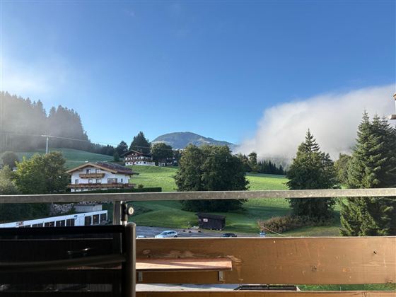 Een mooi uitzicht op een berglandschap met groene weiden en bomen. Op de achtergrond zijn er zachte heuvels en lage wolken te zien.