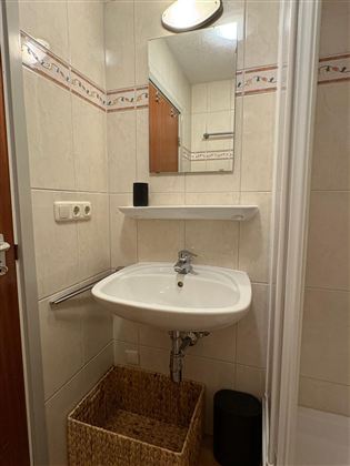 Een kleine badkamer met een wastafel en een spiegel. Aan de muur zijn lichte tegels en een douchecabine zichtbaar.