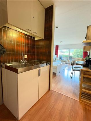 Een moderne keuken met een gootsteen en houten planken. Op de achtergrond is een gezellige woonkamer met een tafel en stoelen te zien.