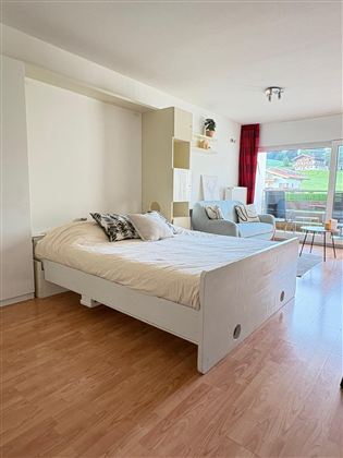 Een gezellige slaapkamer met een open bed en een comfortabele stoel. Grote ramen zorgen voor veel daglicht en een uitzicht op de omgeving.