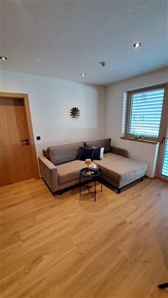 Ein gemütliches Wohnzimmer mit einem bequemen Sofa und einem kleinen Tisch. Das Licht fällt durch das Fenster und schafft eine einladende Atmosphäre.